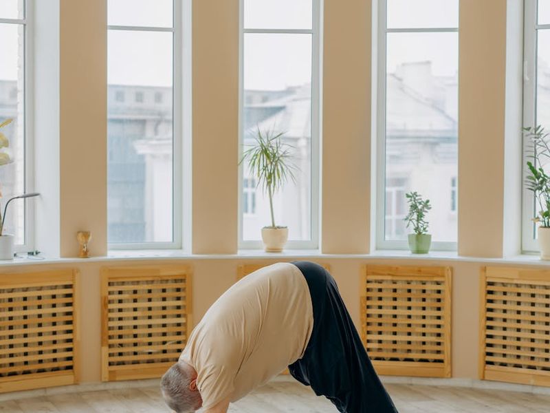 Person practicing yoga in a spacious, bright studio with large windows.